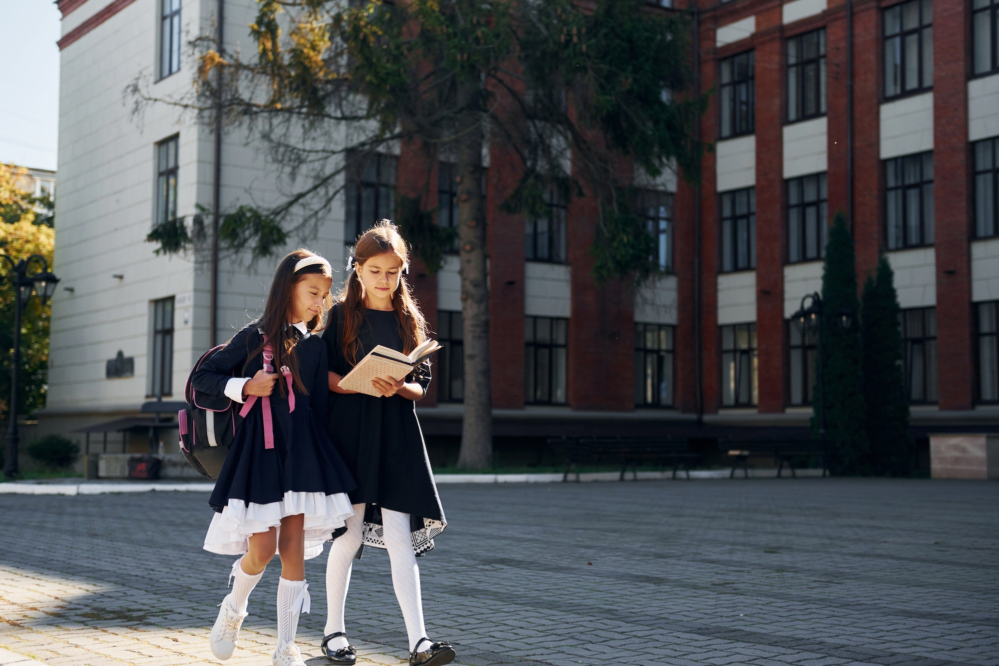 With books. Two schoolgirls is outside together near school building